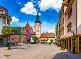 Ein Ausblick auf einen idyllischen Marktplatz am Tag mit einer Kirche, mehreren Fahnen und Geschäften