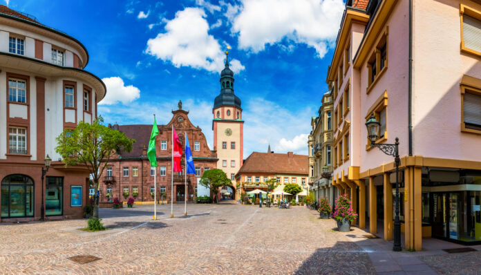 Ein Ausblick auf einen idyllischen Marktplatz am Tag mit einer Kirche, mehreren Fahnen und Geschäften