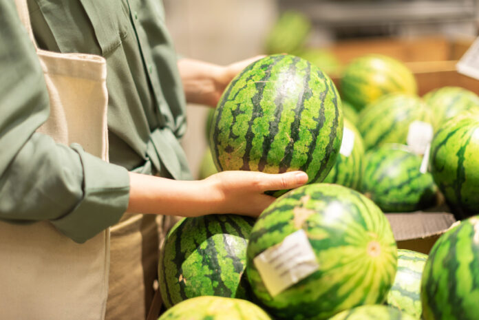 Eine Kundin wählt in der Obstabteilung eines Supermarktes eine Wassermelone aus.