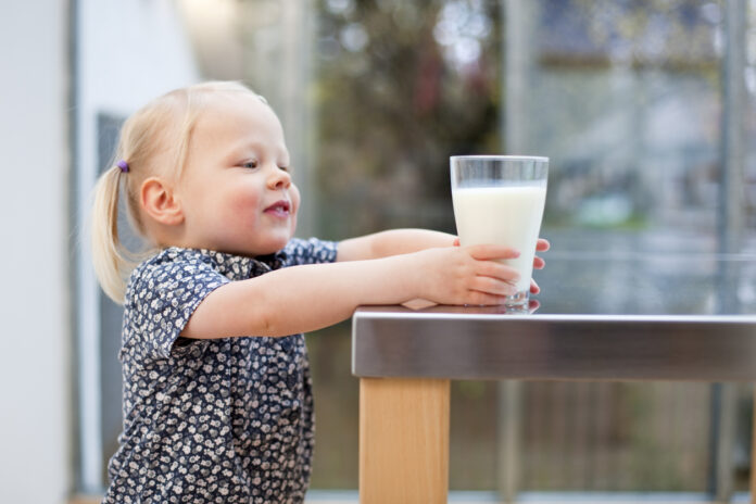 Ein kleines Mädchen greift nach einem Glas Milch.