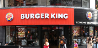 Eine Burger King Filiale an einer Ecke. Davor sammeln sich viele Menschen und drinnen gibt es eine lange Schlange an der Kasse.