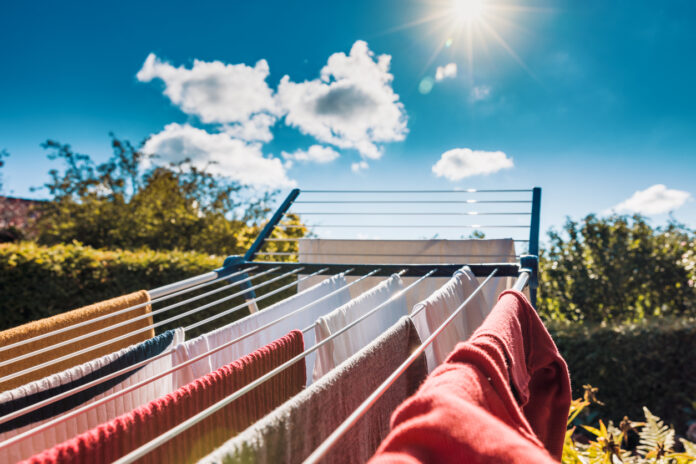 Die Wäsche hängt auf einer Leine im Garten. Jemand hat die Wäsche im Freien aufgehängt, hier soll sie trocknen. Pullover, T-Shirts und Hosen hängen draußen, so trocknen die Textilien schneller.