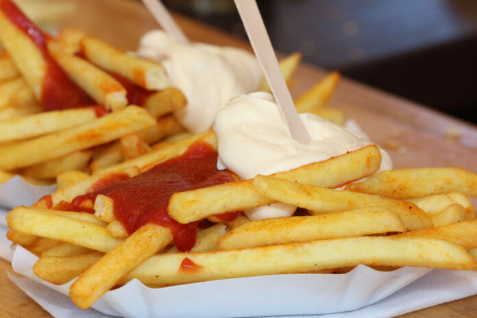 Auf einem Tisch befinden sich zwei Portionen Pommes mit Ketchup und Mayonnaise. Die Schalen sind gut gefüllt. In einem Ort erreichen die Pommes nun die 7-Euro-Marke.