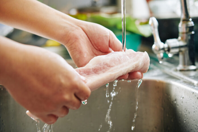 Ein Stück Hähnchenbrust wird über der Spüle mit Wasser gewaschen