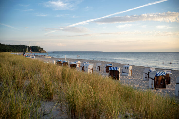 An einem Strand der Ostsee stehen zahlreiche Strandkörbe auf dem Sand. Dahinter liegt das Meer und der weite Horizont mit vereinzelt dünnen Wolken.