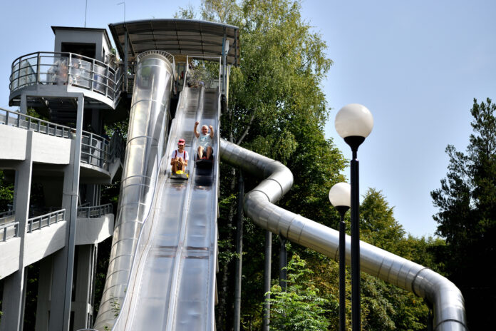 Opa und Enkelin rutschen eine Riesen-Rutsche runter in einem XXL-Park.