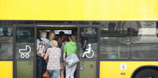 Viele Menschen quetschen sich in einen gelben Bus.