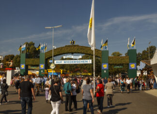 Viele Menschen gehen auf ein Tor mit der Aufschrift "Auf Wiedersehen" zu. Es ist der Ausgang des Freizeitparks Phantasialand. Die Sonne scheint.