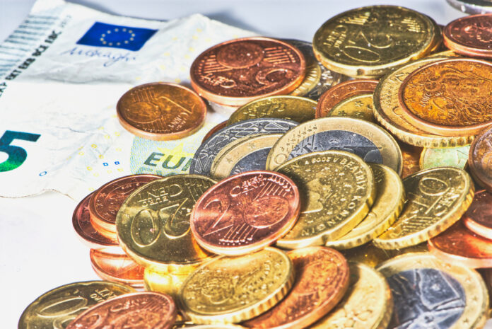 Euro-Münzen und 5-Euro-Schein. In dem Haufen befinden sich Münzen von verschiedenem Wert mit ein Cent, 2-Cent, 1-Euro- und 2-Euro Stücke. Darunter befinden sich mehrere 5-Euro-Scheine.