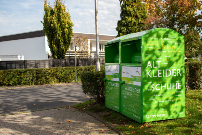 Ein grüner Kleidercontainer steht an einem Weg.