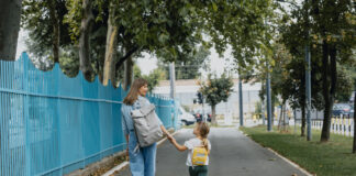 Eine Mutter holt ihr Kind von der Kita ab. Sie gehen gemeinsam einen Weg entlang und sind auf dem Weg nach Hause. Die kleine Familie sieht glücklich aus.