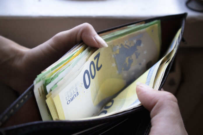 Eine Frau hält in ihren Händen ein Portemonnaie mit vielen Geldscheinen. Eine Million Deutsche erhalten nun einen Zuschuss.