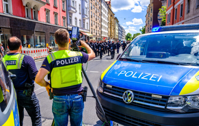 Polizisten sind bei einem Einsatz in der Innenstadt zu sehen. Ein Streifenwagen steht mit Beamten in Warnwesten auf der Straße, während vor ihnen eine Demonstration sich bewegt.