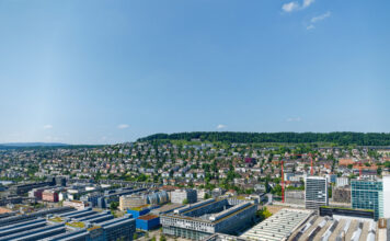 Eine Luftaufnahme eines Gewerbegebiets. Man sieht verschiedene Bauwerke in einem Industriegebiet. Darunter sind Hallen und Werke von großen Konzernen und Unternehmen.