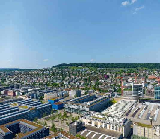 Eine Luftaufnahme eines Gewerbegebiets. Man sieht verschiedene Bauwerke in einem Industriegebiet. Darunter sind Hallen und Werke von großen Konzernen und Unternehmen.