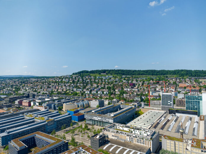 Eine Luftaufnahme eines Gewerbegebiets. Man sieht verschiedene Bauwerke in einem Industriegebiet. Darunter sind Hallen und Werke von großen Konzernen und Unternehmen.