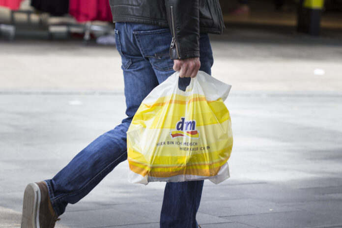 Eine Person trägt eine Plastiktüte von dm nach einem Einkauf über die Straße