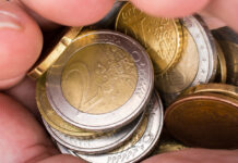 Eine Person hat die Hände voller Münzen. Darunter sind 2-Euro-Stücke, 20-Cent-Münzen und 10-Cent-Münzen. Das Kleingeld strahlt in gold und silber.