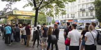 Menschenschlange vor einem türkischen Imbiss. Die Kunden warten darauf, ihren Döner bestellen zu können. Die Gäste stehen in einer schier endlosen Schlange auf dem Bordstein. Im Hintergrund prangt das Zeichen "Mustafas Gemüsedöner".