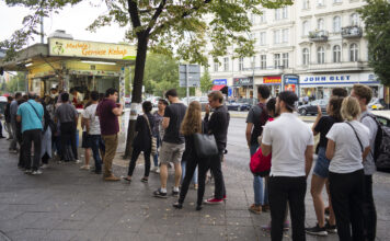 Menschenschlange vor einem türkischen Imbiss. Die Kunden warten darauf, ihren Döner bestellen zu können. Die Gäste stehen in einer schier endlosen Schlange auf dem Bordstein. Im Hintergrund prangt das Zeichen "Mustafas Gemüsedöner".