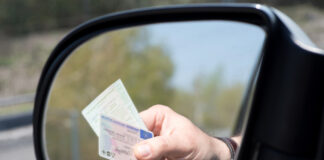 Ein Mann zeigt seinen Führerschein vor und seine Zulassungsbescheinigung vor. Wahrscheinlich befindet er sich in einer Polizeikontrolle. Er reicht seine Dokumente aus dem Fahrerfenster. Zu sehen ist seine Hand mit den Dokumenten im Seitenspiegel.