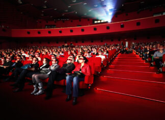 Mehrere Menschen sitzen in einem Kinosaal und schauen einen Film. Die roten Sitze im Kino bieten den Gästen jede Menge Komfort und Platz.