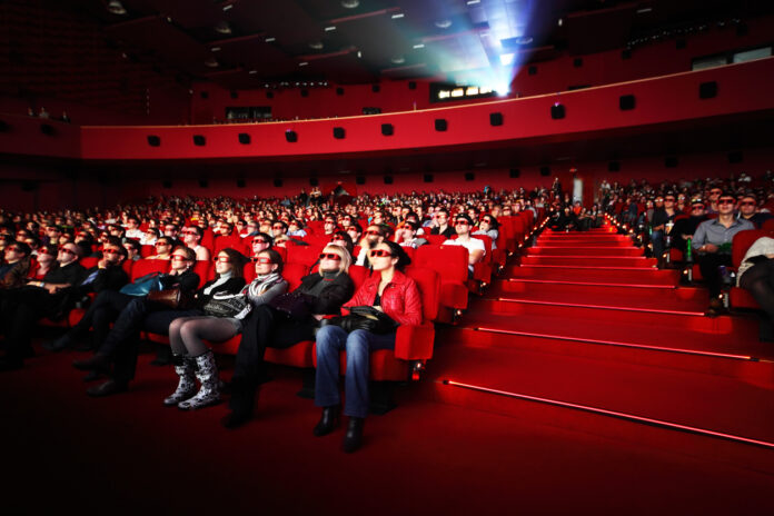 Mehrere Menschen sitzen in einem Kinosaal und schauen einen Film. Die roten Sitze im Kino bieten den Gästen jede Menge Komfort und Platz.