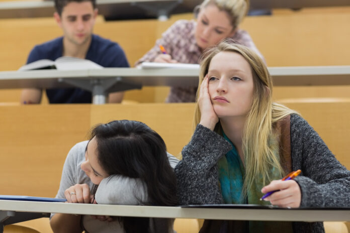 Eine Studentin sitzt an ihrem Platz und verfolgt gelangweilt und müde eine Vorlesung