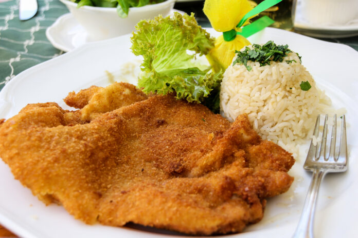 Ein Schnitzel liegt mit Reis und Salat auf einem Teller.