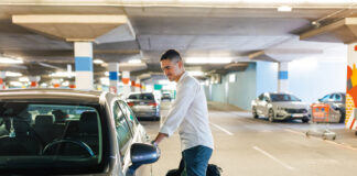 Ein Mann öffnet die Autotür seines Fahrzeugs in einem Parkhaus auf dem Parkplatz. Im Hintergrund stehen andere Autos in der Garage.