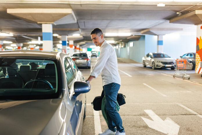 Ein Mann öffnet die Autotür seines Fahrzeugs in einem Parkhaus auf dem Parkplatz. Im Hintergrund stehen andere Autos in der Garage.