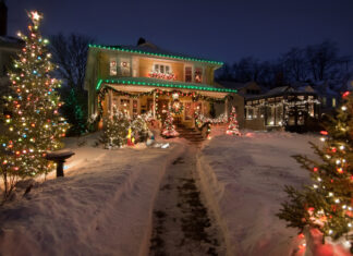 Ein geschmücktes Haus mit Weihnachtsdeko. Daneben steht ein Weihnachtsbaum und davor liegt Schnee.