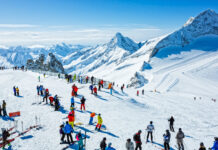 Unzählige Touristen fahren Ski und Snowboard in den Bergen. Es ist sonnig und sie machen Wintersport im Winterurlaub in einem Skigebiet im Schnee. Sie haben bunte Jacken an gegen die Kälte.