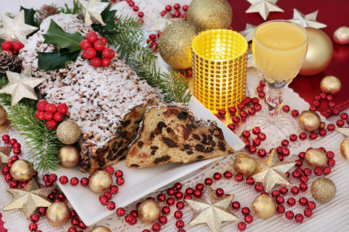 Zwischen weihnachtlicher Deko liegt ein Weihnachtsstollen auf einem Teller und es steht ein Glas Eierlikör dabei