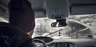 Ein Mann fährt mit einer Mütze im Auto. Draußen liegt Schnee.