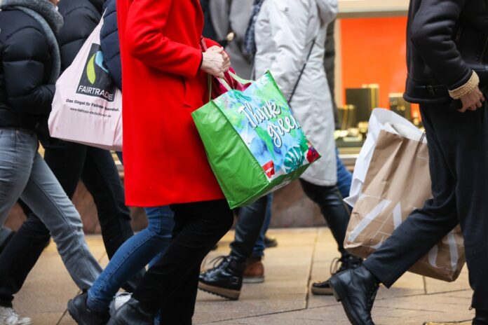 Mehrere Kunden mit Geschenktüten laufen durch eine Innenstadt, sie waren einkaufen