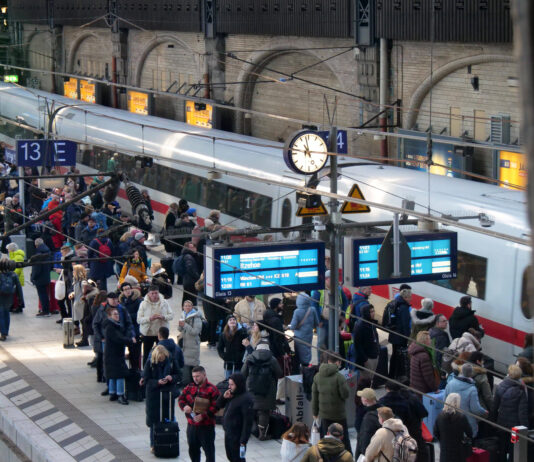 Viele Menschen tummeln sich an einem Bahnsteig, an dem ein Zug steht.