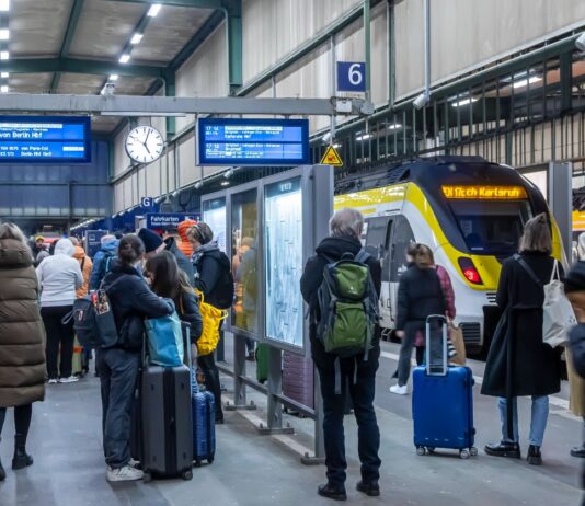 Mehrere Fahrgäste stehen am Bahnsteig und warten auf die Abfahrt des Zuges