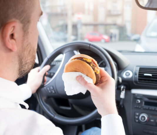 Ein Mann isst einen Burger im Auto.