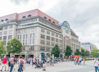 Ein großes Gebäude des KaDeWe in einer Innenstadt, an dem einige Menschen vorbeilaufen und andere hineingehen. Es ist ein schöner sonniger Tag.