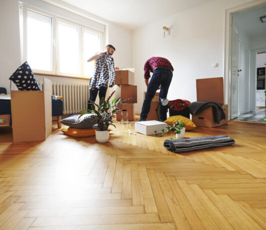 Zwei Männer räumen für den Umzug die Wohnung leer. Mehrere Kartons stehen in dem fast leeren Wohnzimmer sowie eine Topfpflanze. Die Wände sind weiß, der Parkettboden im Holz-Design. Wer gegen ein bestimmtes Verbot in Wohnungen verstößt, muss mit einer saftigen Strafe rechnen.