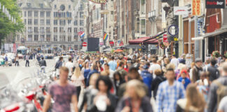 Zahlreiche Menschen drängen sich in einer Einkaufsstraße mitten in der Innenstadt. Das Foto ist verwaschen, jedoch erkennt man viele junge und alte Bürger sowie dutzende Geschäfte, Fassenden, Cafés und den gesamten Trubel der Straße in der Innenstadt.