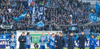 Die Spieler des Karlsruher SC stehen gemeinsam auf dem Rasen des Wildparkstadions in Karlsruhe. Die Fans in den Zuschauer-Rängen jubeln ihnen zu nach einem erfolgreichen Fußballspiel in der 2. Bundesliga.