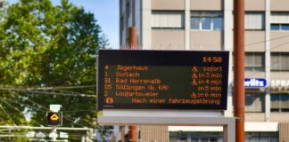 Alle Abfahrtszeiten einer Haltestelle sind auf einer digitalen Tafel vermerkt. In oranger Schrift leuchten die Zeiten, zu denen die einzelnen Linien des öffentlichen Nahverkehrs in einer deutschen Stadt fahren.