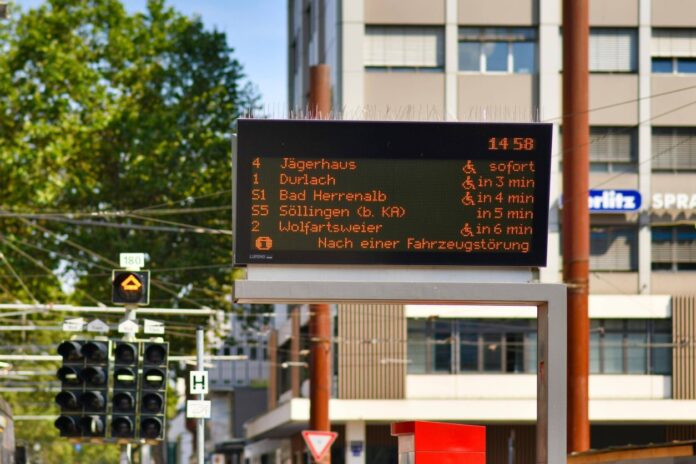 Alle Abfahrtszeiten einer Haltestelle sind auf einer digitalen Tafel vermerkt. In oranger Schrift leuchten die Zeiten, zu denen die einzelnen Linien des öffentlichen Nahverkehrs in einer deutschen Stadt fahren.