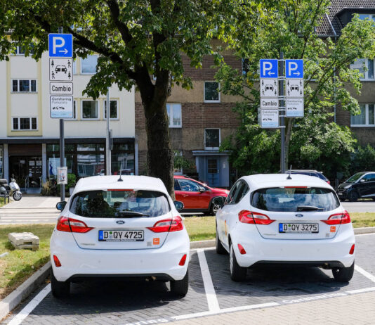 Zwei Wagen einer Autovermietung stehen auf einem Parkplatz. Sie parken auf dieser Fläche vor einem Parkautomaten und den Verkehrsschildern, welche darauf hinweisen.