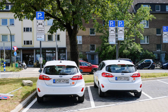 Zwei Wagen einer Autovermietung stehen auf einem Parkplatz. Sie parken auf dieser Fläche vor einem Parkautomaten und den Verkehrsschildern, welche darauf hinweisen.