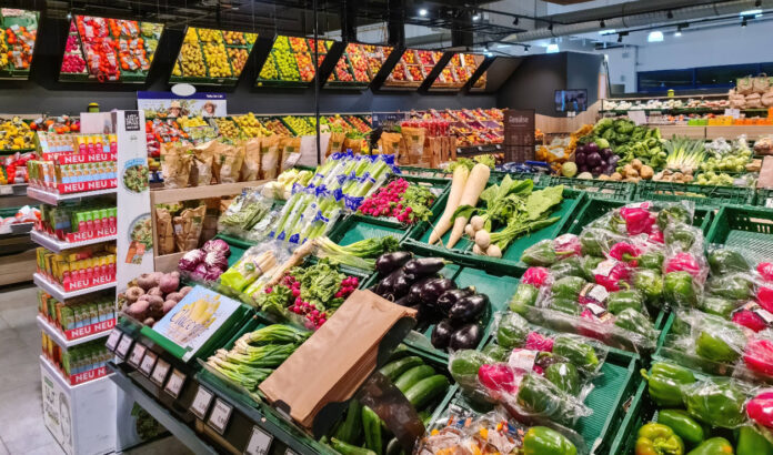 Eine Obst- und Gemüseabteilung in einem Supermarkt. In der Abteilung gibt es eine große Auswahl an verschiedenem Obst und Gemüse, das frisch aufgestapelt ist.