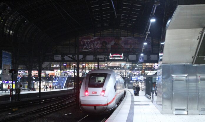 Ein Zug hält an einem Bahnsteig auf einem Bahnhof in der Nacht und Fahrgäste steigen ein