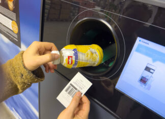 Eine Frau legt mit der linken Hand eine Milchflasche in den Pfandautomaten und in der rechten hält sie einen Pfandbon in der Hand.